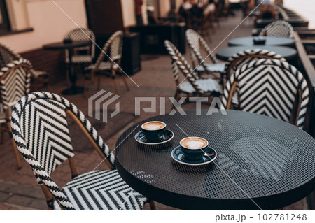 Two beautiful cups of cappuccino on the table on city background. Perfect heart shape latte art. Coffee break, time in cafe, relax and enjoy the hot drink concept. Side view. Copy space for your text. 102781248