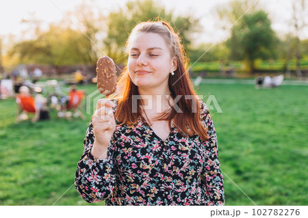 Happy young woman with delicious chocolate ice cream outdoors. Unhealhty food and weight loss concept. Summer time, eating Happy young woman with delicious chocolate ice cream outdoors. Unhealhty food and weight loss concept. Summer time, eating 102782276