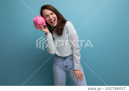 cute 20s brunette lady in shirt and jeans saved up her money for a dream in a piggy bank 102786057
