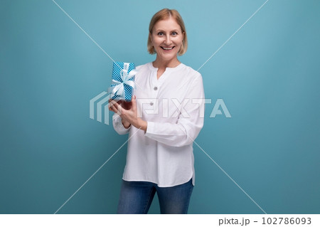 blond mature woman holding gift box on studio background 102786093