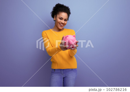 pretty joyful 20s latin woman with afro hair in casual yellow sweater accumulated money in a piggy pretty joyful 20s latin woman with afro hair in casual yellow sweater accumulated money in a piggy 102786216