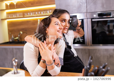 Two funny female chef in uniform holding kitchenware while smiling and having fun at camera in the kitchen 102786996