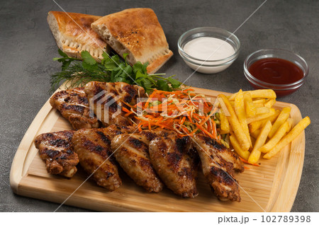 grilled chicken wings with french fries, salad and sauces on a wooden board 102789398