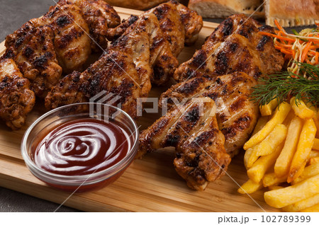 grilled chicken wings with french fries, salad and sauces on a wooden board grilled chicken wings with french fries, salad and sauces on a wooden board 102789399