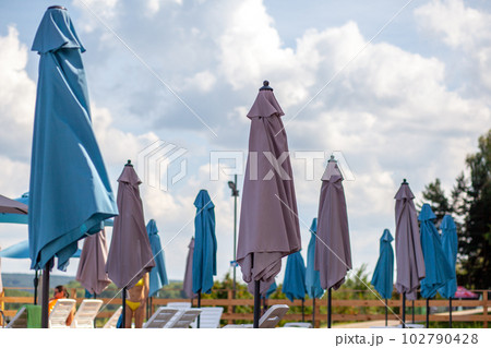 Folded beach umbrellas. Preparing the beach for the new opening season. Lots of beach umbrellas next to the water pool. The concept of tourist vacation and vacation. Folded beach umbrellas. Preparing the beach for the new opening season. Lots of beach umbrellas next to the water pool. The concept of tourist vacation and vacation. 102790428