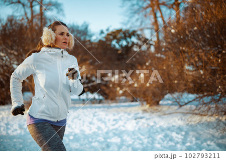 active woman in white jacket with ear warmer jogging active woman in white jacket with ear warmer jogging 102793211