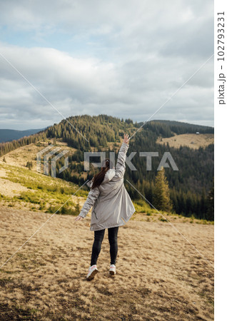 Happy girl stands in the mountains, enjoys the beautiful view and raises her hand up 102793231