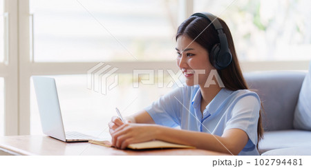 Online education, e-learning. Asian woman in stylish casual clothes, studying using a laptop, listening to online lecture, taking notes, online study at home Online education, e-learning. Asian woman in stylish casual clothes, studying using a laptop, listening to online lecture, taking notes, online study at home 102794481
