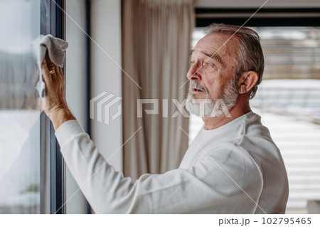 Senior man cleaning windows in his house. Senior man cleaning windows in his house. 102795465