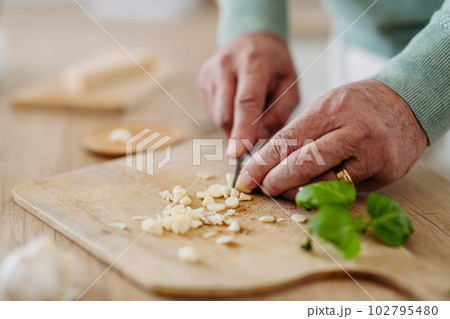 Close up of senior man cutting garlic. Close up of senior man cutting garlic. 102795480