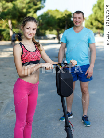 Girl riding kick scooter with father Girl riding kick scooter with father 102797540