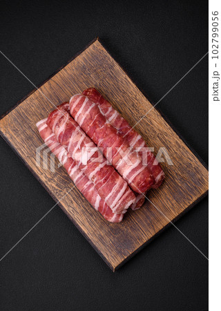 Raw minced meat wrapped in bacon with salt and spices or cevapcici Raw minced meat wrapped in bacon with salt and spices or cevapcici 102799056