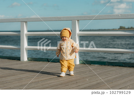 A toddler in a yellow jacket and pants walks on the pier 102799129