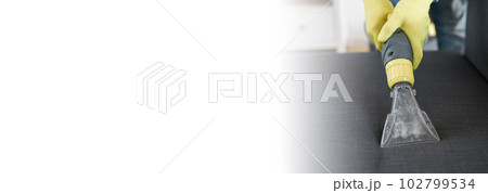 Man dry cleaner's employee hand in protective rubber glove cleaning sofa with professionally extraction method. Early spring regular cleanup. Commercial cleaning company concept Man dry cleaner's employee hand in protective rubber glove cleaning sofa with professionally extraction method. Early spring regular cleanup. Commercial cleaning company concept 102799534