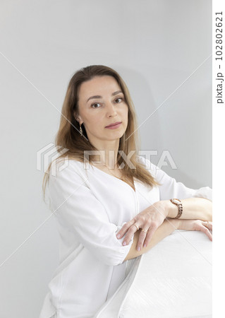 Portrait of Charming Beautician in White Lab Coat Looking at Camera With Smile, Near Couch, Looking at Camera in Spa Salon. Vertical Plane 102802621