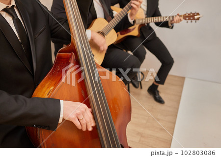 Concert view of a contrabass violoncello player with vocalist and musical band during jazz orchestra band performing music, violoncellist cello jazz player on stage. 102803086