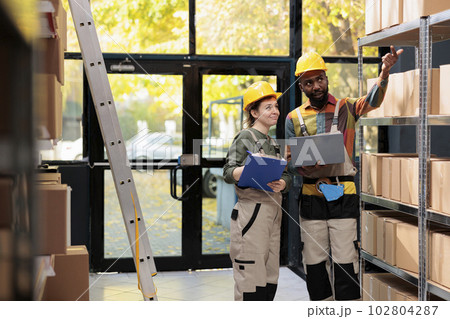 Diverse workers looking at cardboard boxes during inventory, preparing packages for customers orders. Small business employees working at delivery process analyzing checklist on laptop Diverse workers looking at cardboard boxes during inventory, preparing packages for customers orders. Small business employees working at delivery process analyzing checklist on laptop 102804287