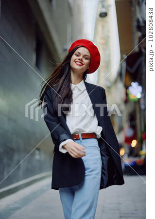 Fashion woman smile with teeth portrait walking tourist in stylish clothes in jacket with red lips walking down narrow city street flying hair, travel, cinematic color, retro vintage style. 102808438