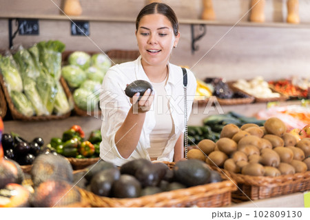 Smiling young girl choosing avocados while shopping in supermarket 102809130