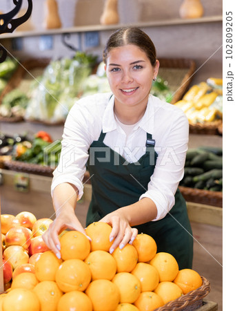 Young saleswoman laying out oranges on display supermarket 102809205