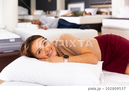 Happy young hispanic woman testing mattress in furniture showroom Happy young hispanic woman testing mattress in furniture showroom 102809537