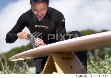 サーフボードにフィンを取り付けるウェットスーツ姿の男性 102812317