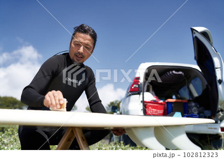 サーフボードにワックスをつけるサーファーの男性 102812323