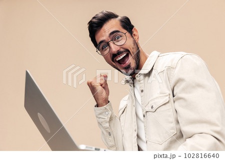 Portrait of a stylish man smile with teeth with a laptop in the hands of a freelancer, on a beige background in a white t-shirt, fashionable clothing style, space space 102816640