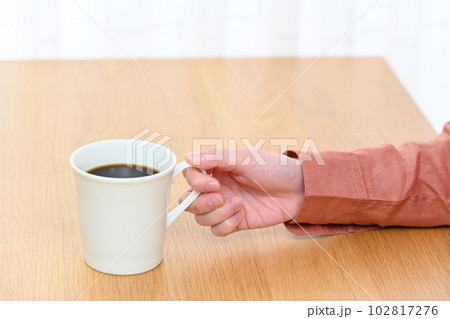 テーブルでコーヒーカップを持つ若い女性の手元 102817276
