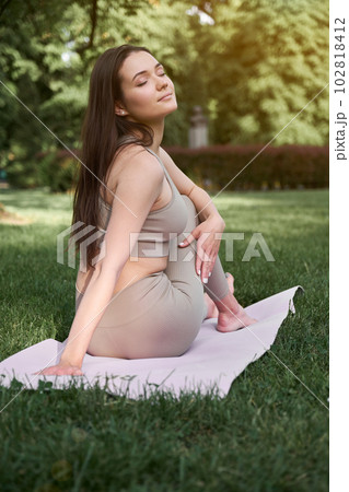 A young woman with a slim figure and long hair practices yoga in the park. Concept of a healthy lifestyle. A young woman with a slim figure and long hair practices yoga in the park. Concept of a healthy lifestyle. 102818412