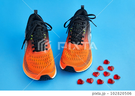 Orange running shoes and red decorative glass hearts scattered on a blue background 102820506