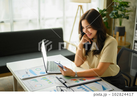 Charming young female entrepreneur smartphone at working desk with laptop and financial documents 102824417
