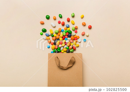 shopping paper gift bag in corner full of assorted traditional candies falling out on colored background with copy space. Happy Holidays sale concept 102825500