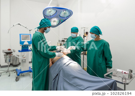 Group of surgeons and nurse in surgical green gown uniform performing surgical operation in operating room. Group of surgeons and nurse in surgical green gown uniform performing surgical operation in operating room. 102826194