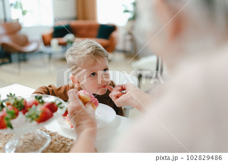 Little boy eating strawberry donut with his grandmother. Little boy eating strawberry donut with his grandmother. 102829486