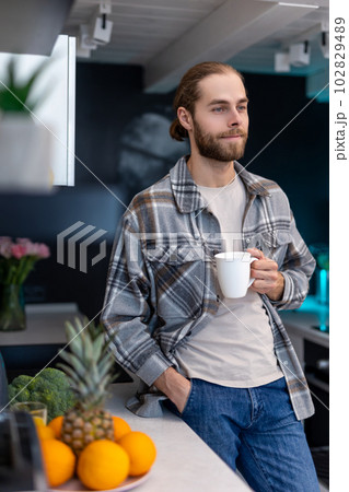 Man enjoying morning coffee in kitchen with modern interior, drinking fresh warm beverage at home. 102829489
