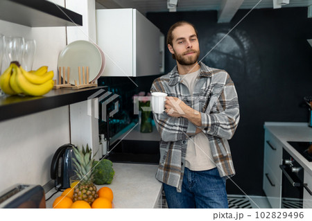 Man enjoying morning coffee in kitchen with modern interior, drinking fresh warm beverage at home. 102829496