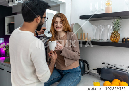 Woman drinking coffee with man while sitting on kitchen counter. Woman drinking coffee with man while sitting on kitchen counter. 102829572