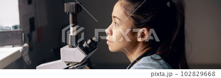 Thoughtful Asian lab assistant sits near microscope looking out of window at workplace 102829668