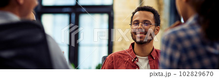 Young smiling mixed race male office worker sitting at the desk and talking with colleagues, working together in the modern office Young smiling mixed race male office worker sitting at the desk and talking with colleagues, working together in the modern office 102829670