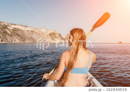 Woman in kayak back view. Happy young woman with long hair floating in kayak on calm sea. Summer holiday vacation and cheerful female people relaxing having fun on the boat. Woman in kayak back view. Happy young woman with long hair floating in kayak on calm sea. Summer holiday vacation and cheerful female people relaxing having fun on the boat. 102830019