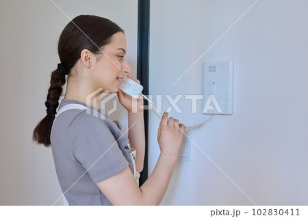 Teenage girl holding intercom handset while talking to guest 102830411