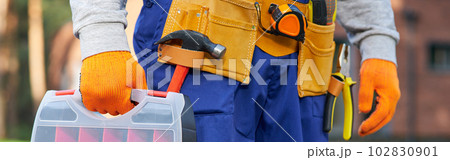 Male builder wearing tool belt carrying toolbox at construction site. Close up on waist area Male builder wearing tool belt carrying toolbox at construction site. Close up on waist area 102830901