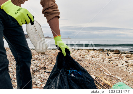 An activist puts a plastic bottle in a garbage bag. The concept of environmental conservation and coastal zone cleaning. An activist puts a plastic bottle in a garbage bag. The concept of environmental conservation and coastal zone cleaning. 102831477