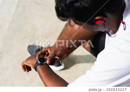 Close up Asian young athlete sport runner black man wear modern time smart watch he sitting resting before training running at the outdoor street health park, healthy exercise before workout concept 102833227