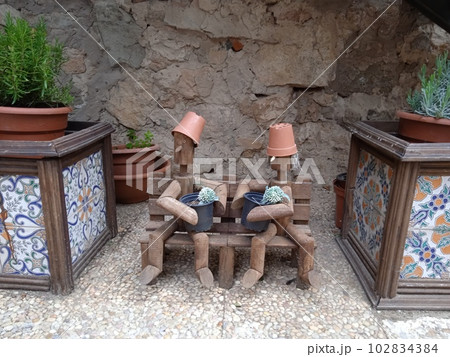 Wooden dolls sitting on a wooden bench. Surrounded by pots. In Medinaceli, in Soria. Photography. Wooden dolls sitting on a wooden bench. Surrounded by pots. In Medinaceli, in Soria. Photography. 102834384
