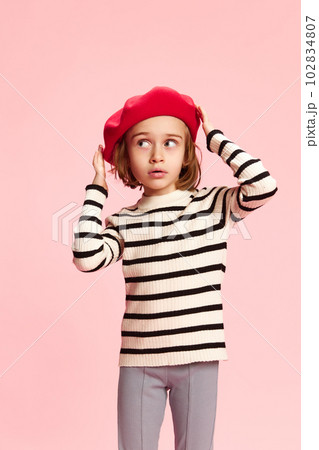 Portrait of beautiful, stylish little girl, child in red beret and striped sweater against pink studio background. Parisian style 102834807