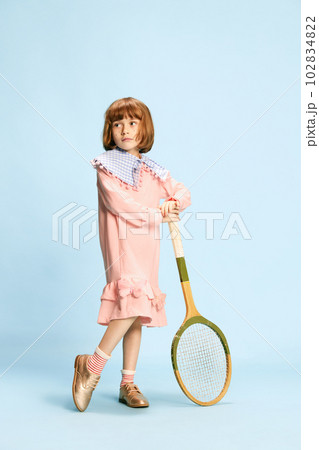 Full-length portrait of pretty little girl in pink dress posing with tennis racket against blue studio background Full-length portrait of pretty little girl in pink dress posing with tennis racket against blue studio background 102834822