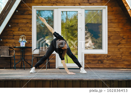 Athletic woman performs bends and spreads her arms to sides during morning workout 102836453