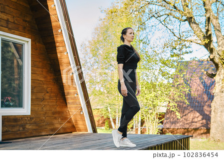 Concentrated woman in tracksuit went out on terrace of wooden house in morning 102836454